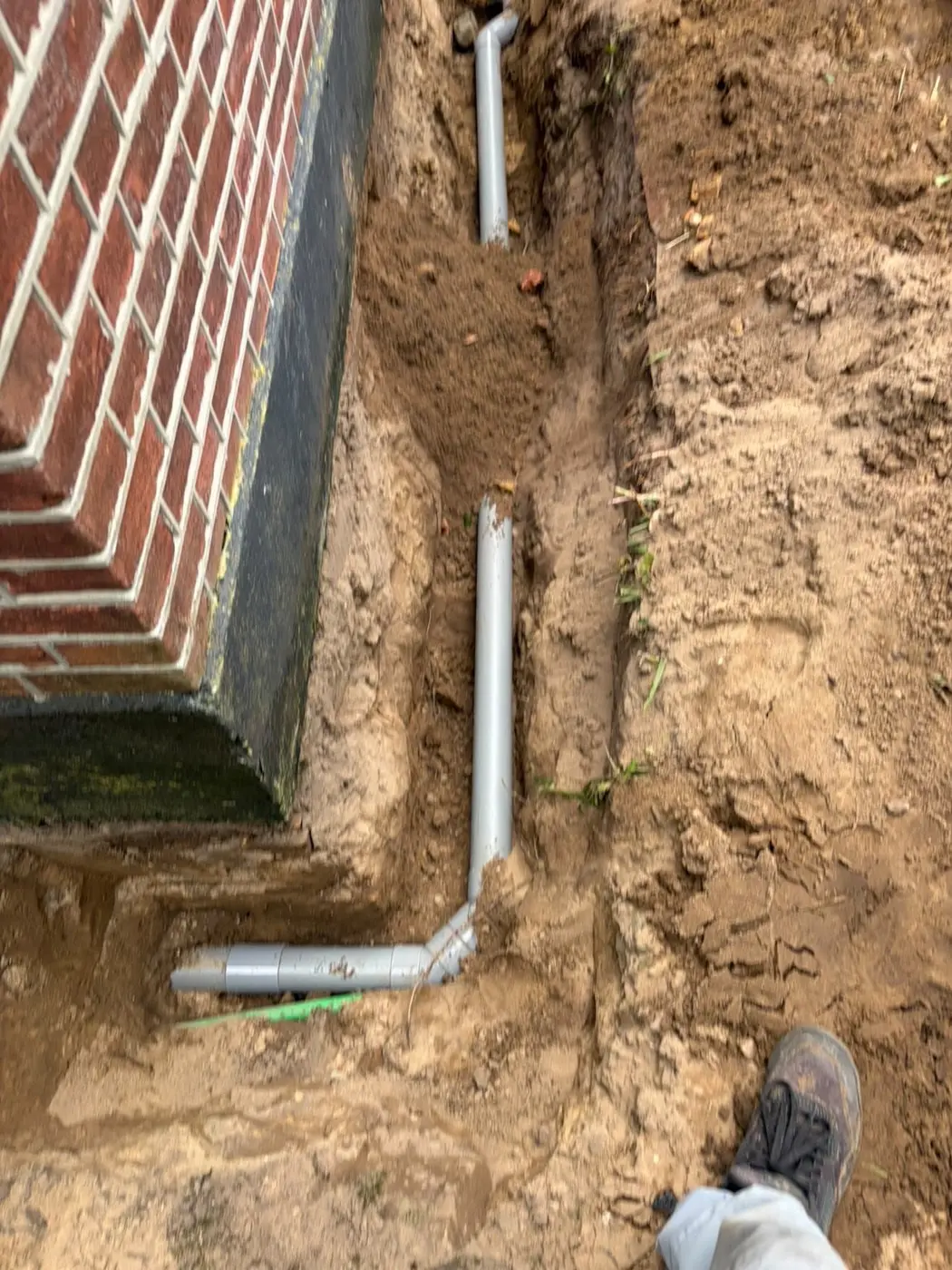 Nieuwe grijze afvoerleiding in uitgegraven grond langs een woning